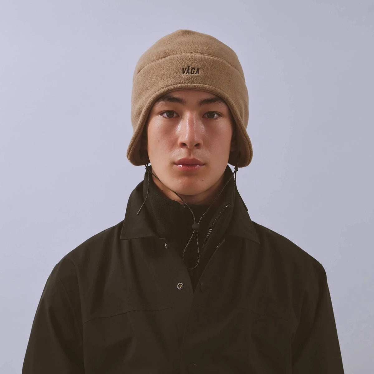 Våga Fleece Summit Beanie in Taupe – getragen, Vorderansicht mit Logo und Ohrenklappen